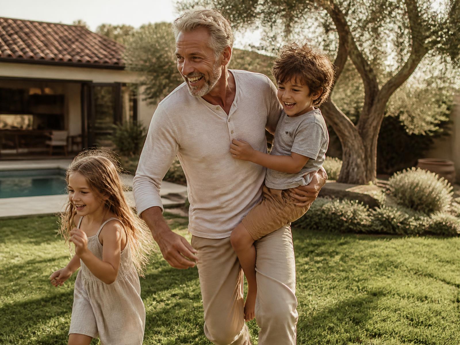A father playing outdoors with his two young children in warm afternoon light